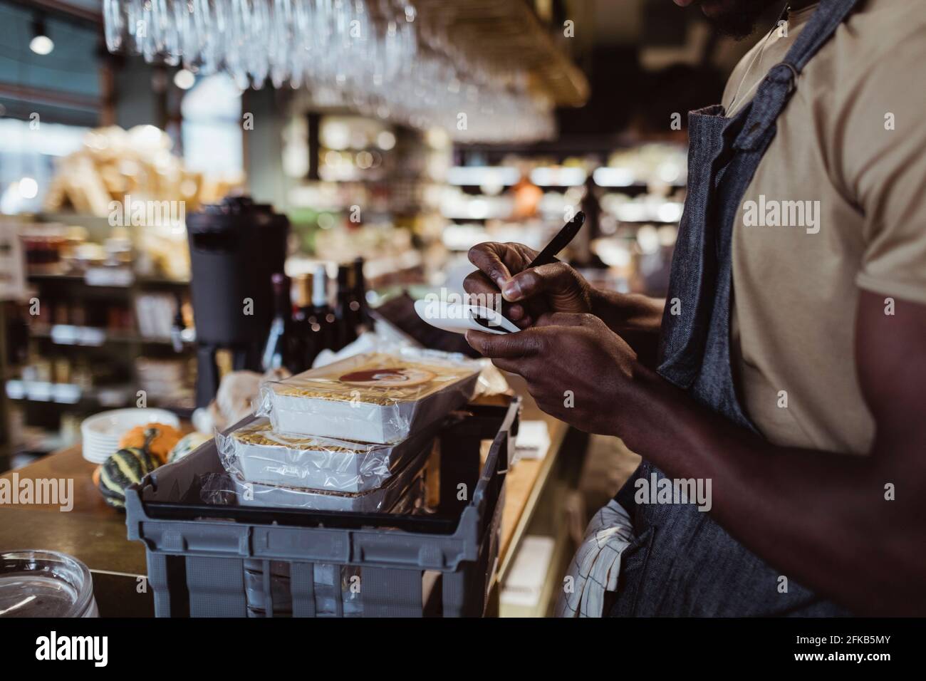 Midsection of male owner writing in note pad at deli store Stock Photo
