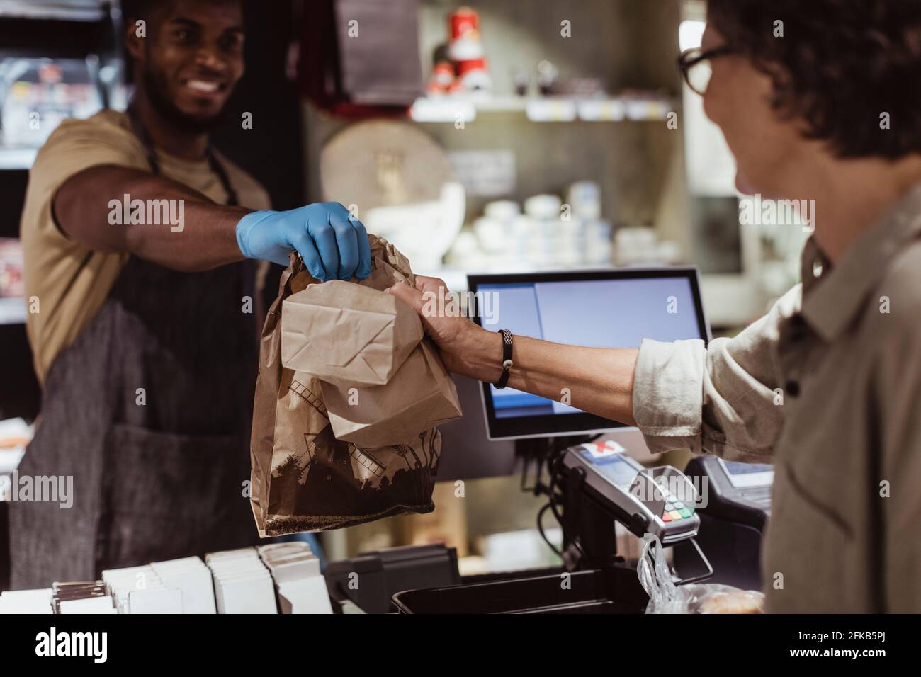 Male owner giving package order to female customer in delicatessen shop Stock Photo