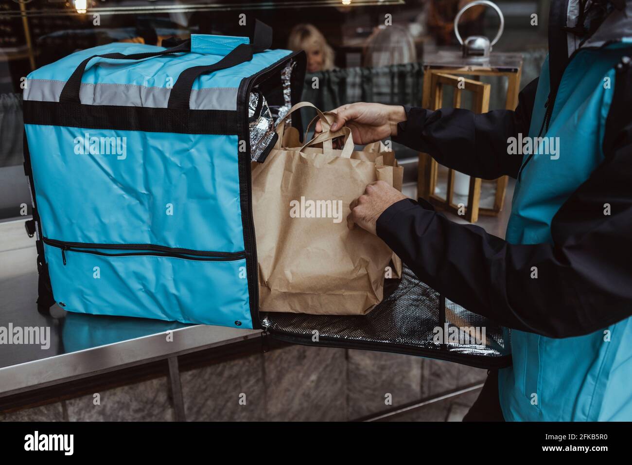 Midsection of delivery man putting package order in backpack outside deli store Stock Photo