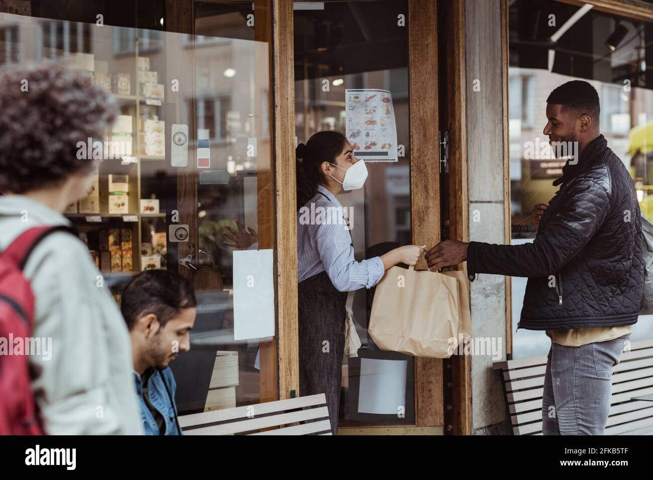 Male customer collecting order from female owner at deli store during pandemic Stock Photo