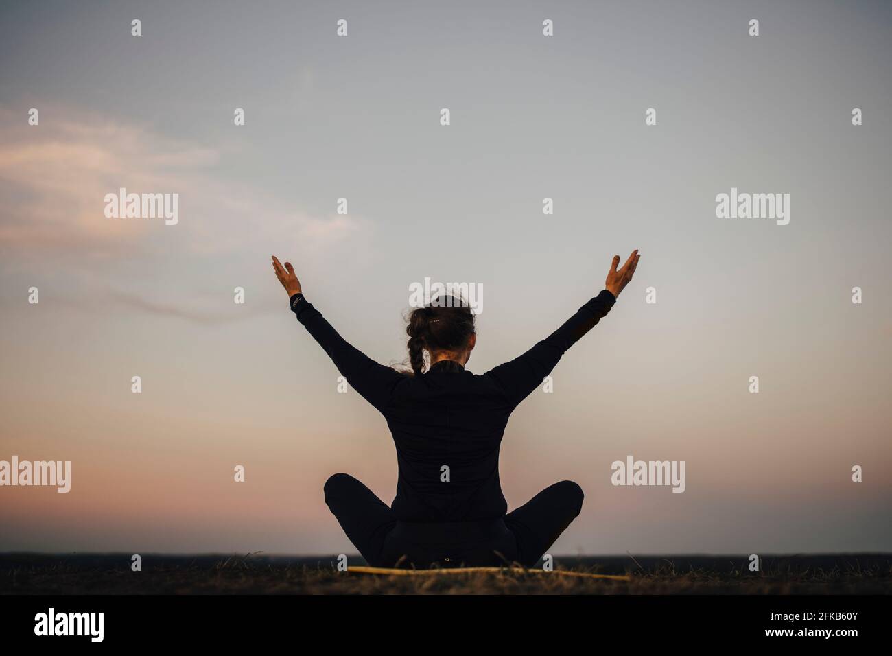 Rear view of sportswoman practicing yoga against sky during sunset Stock Photo