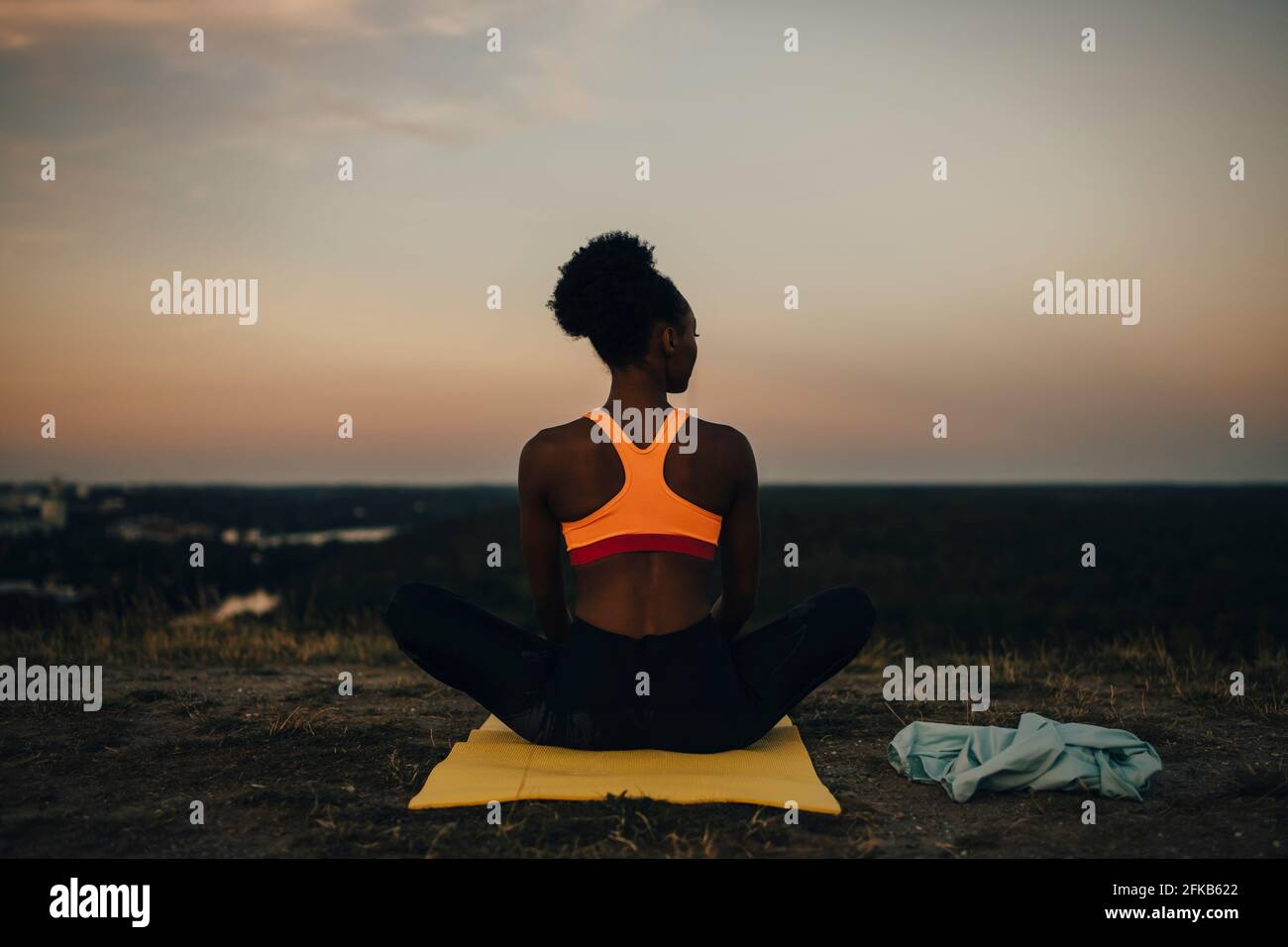 Rear view of sportswoman sitting on exercise mat during sunset Stock Photo