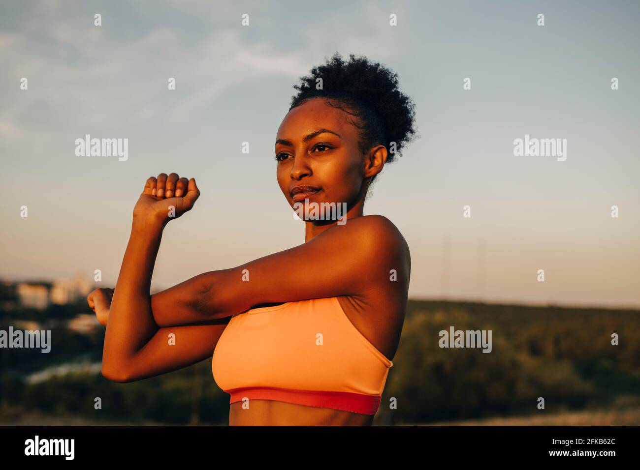Female athlete doing stretching exercise against sky during sunset Stock Photo