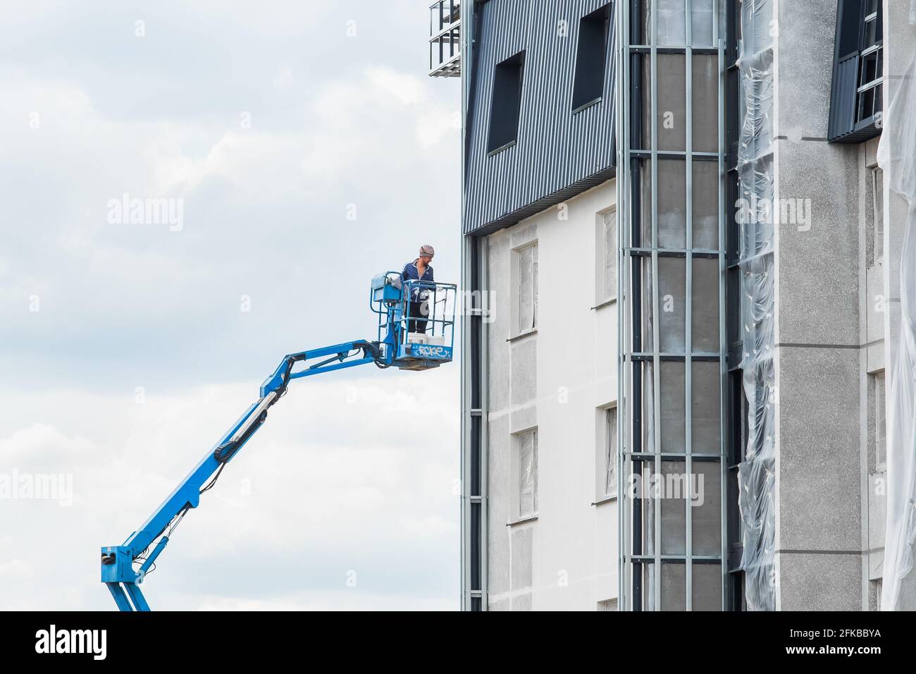 Belarus, Minsk - May 28, 2020: Industrial worker on a lifting platform near a new facade of a house under construction at a construction site. Stock Photo