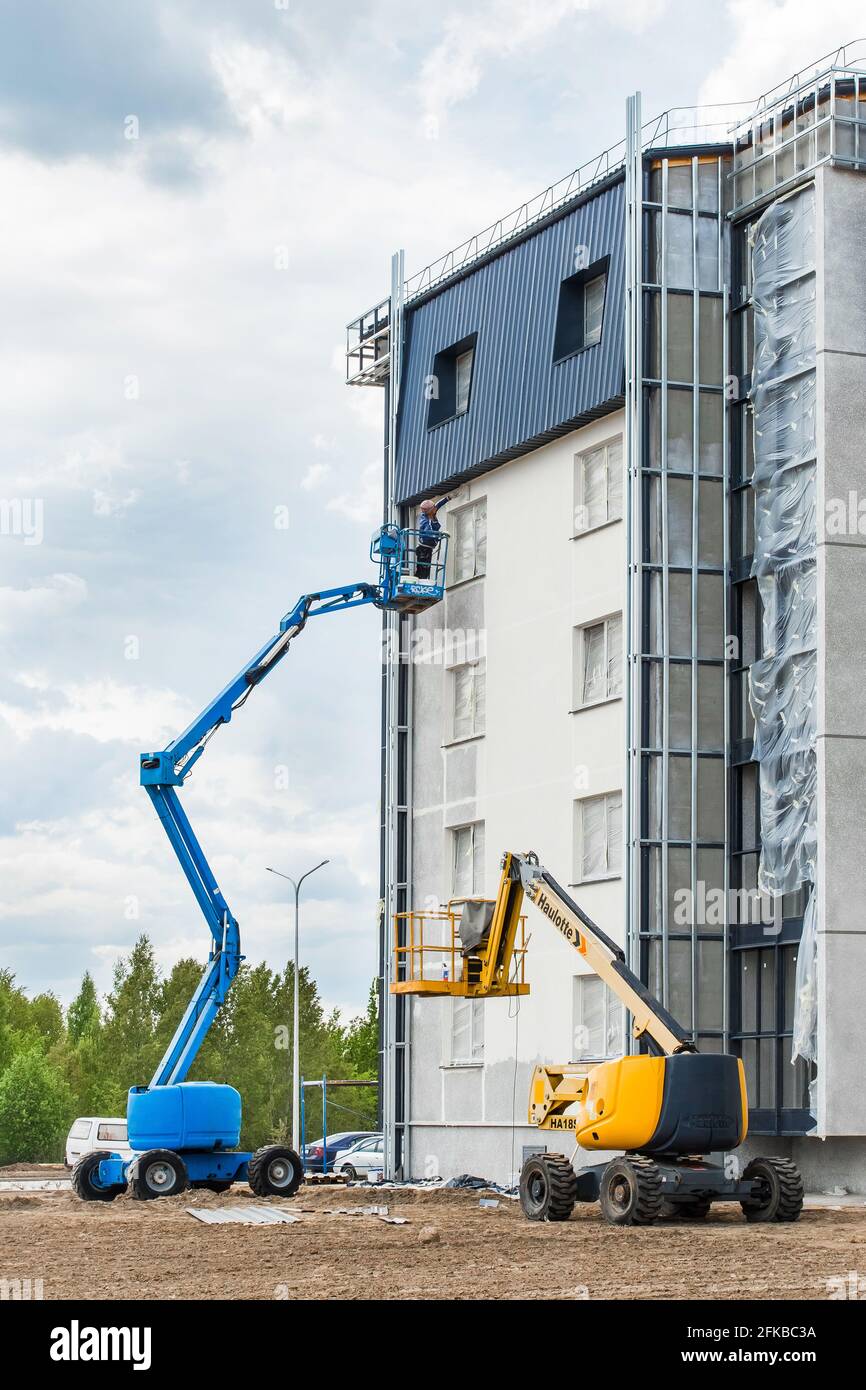 Belarus, Minsk - May 28, 2020: A worker on a lifting platform paints the facade of a new modern urban building under construction at a construction si Stock Photo
