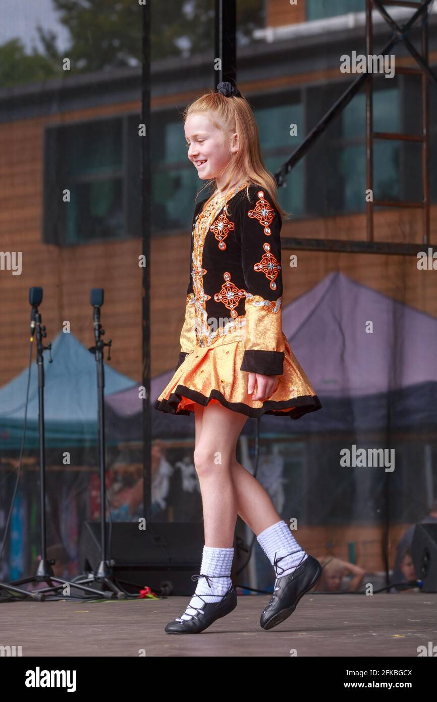 A redheaded Irish dancing girl in a traditional costume performing on stage Stock Photo