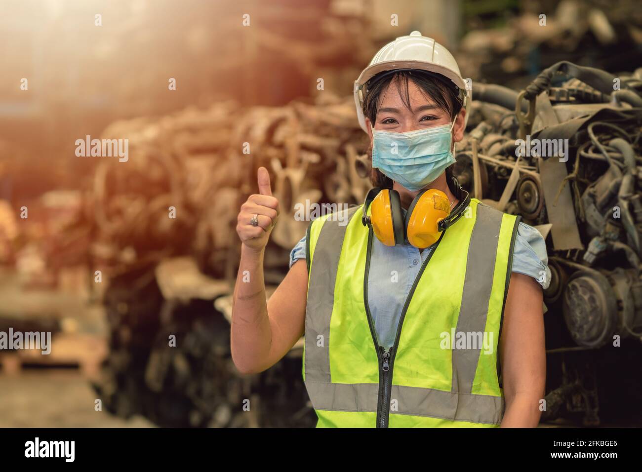 Asian women worker thumbs up waring face mask happy working safety work in a heavy industrial factory with engine machine background Stock Photo