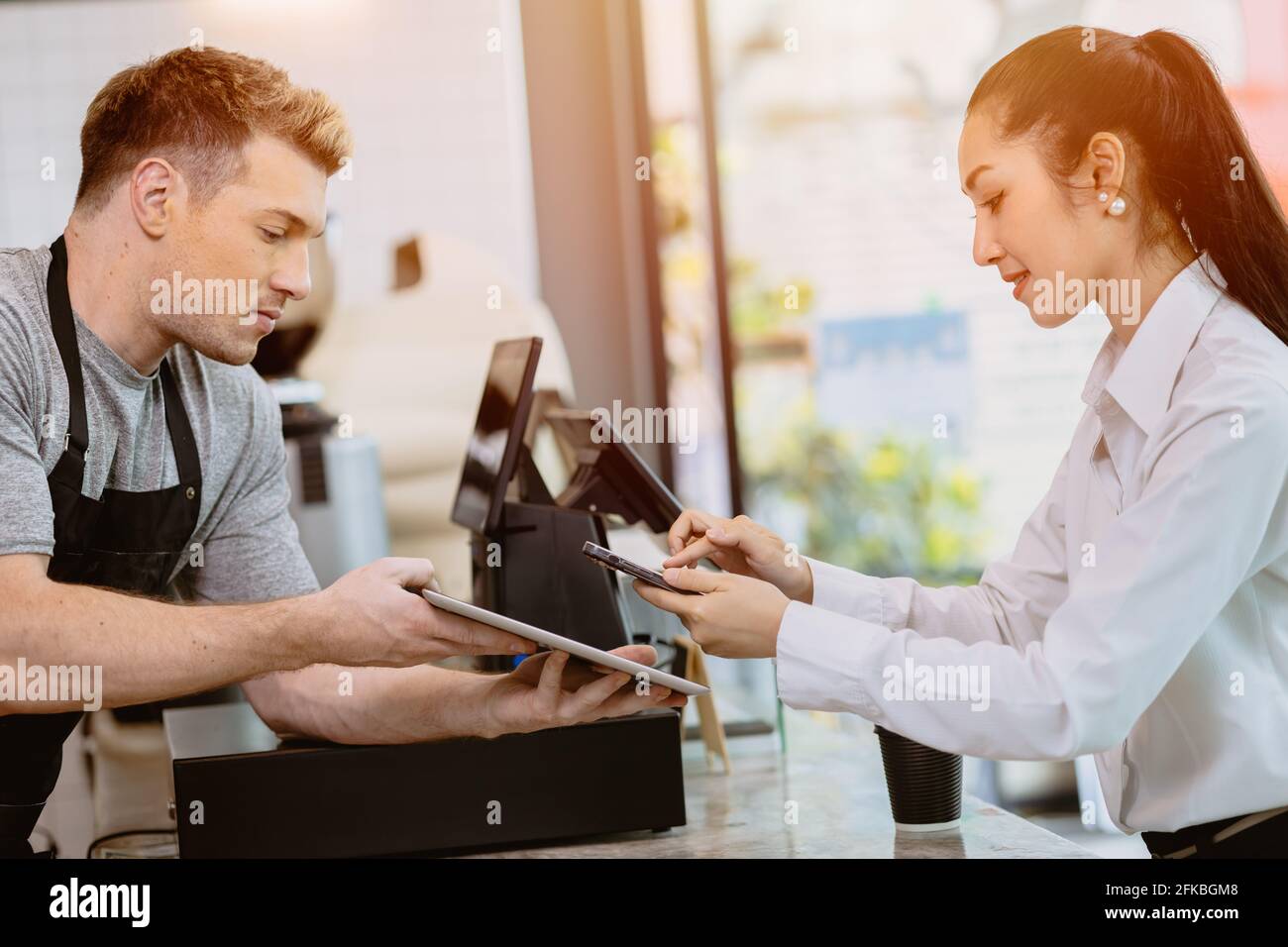 cafe customer using mobile internet banking scan QR payment code for coffee drink from barista staff at the counter, Cashless society modern lifestyle Stock Photo