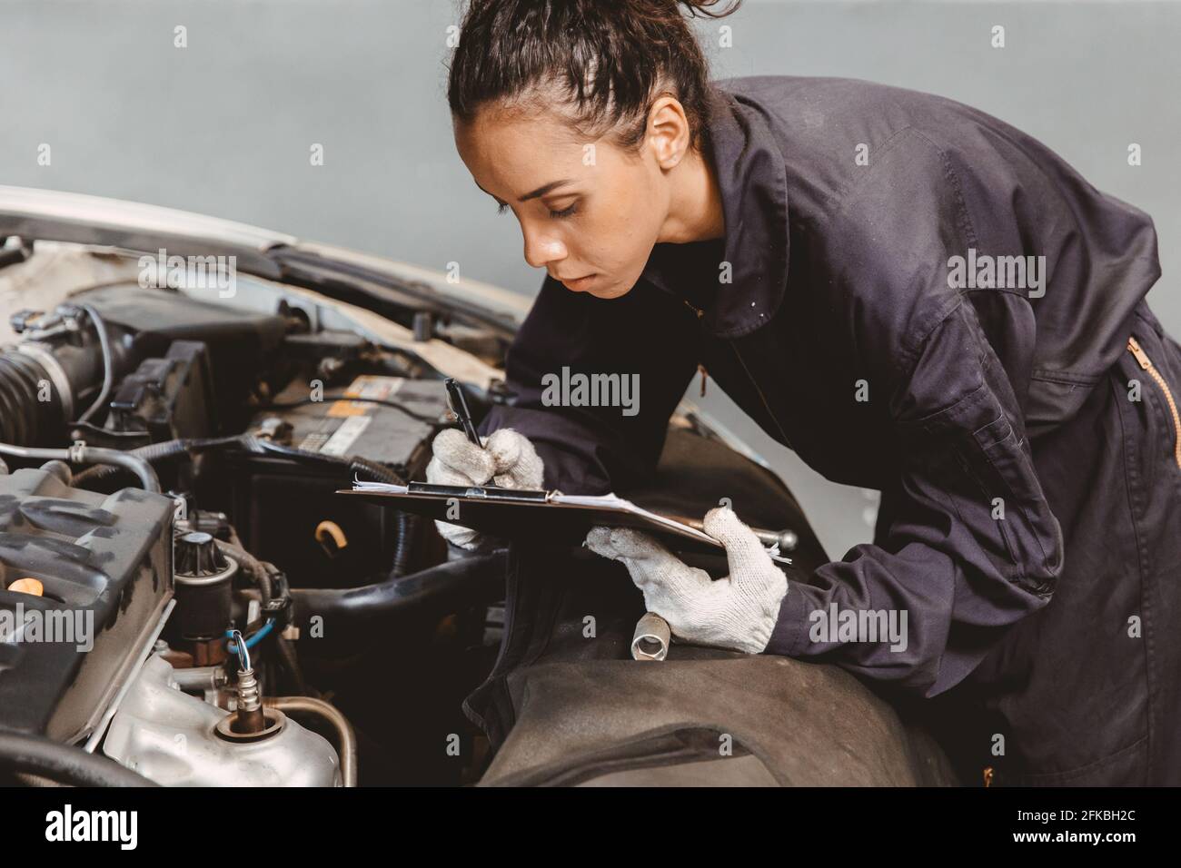 Woman garage worker maintenance checklist at automobile service center, Female in auto mechanic car technician work service check and repair customer Stock Photo