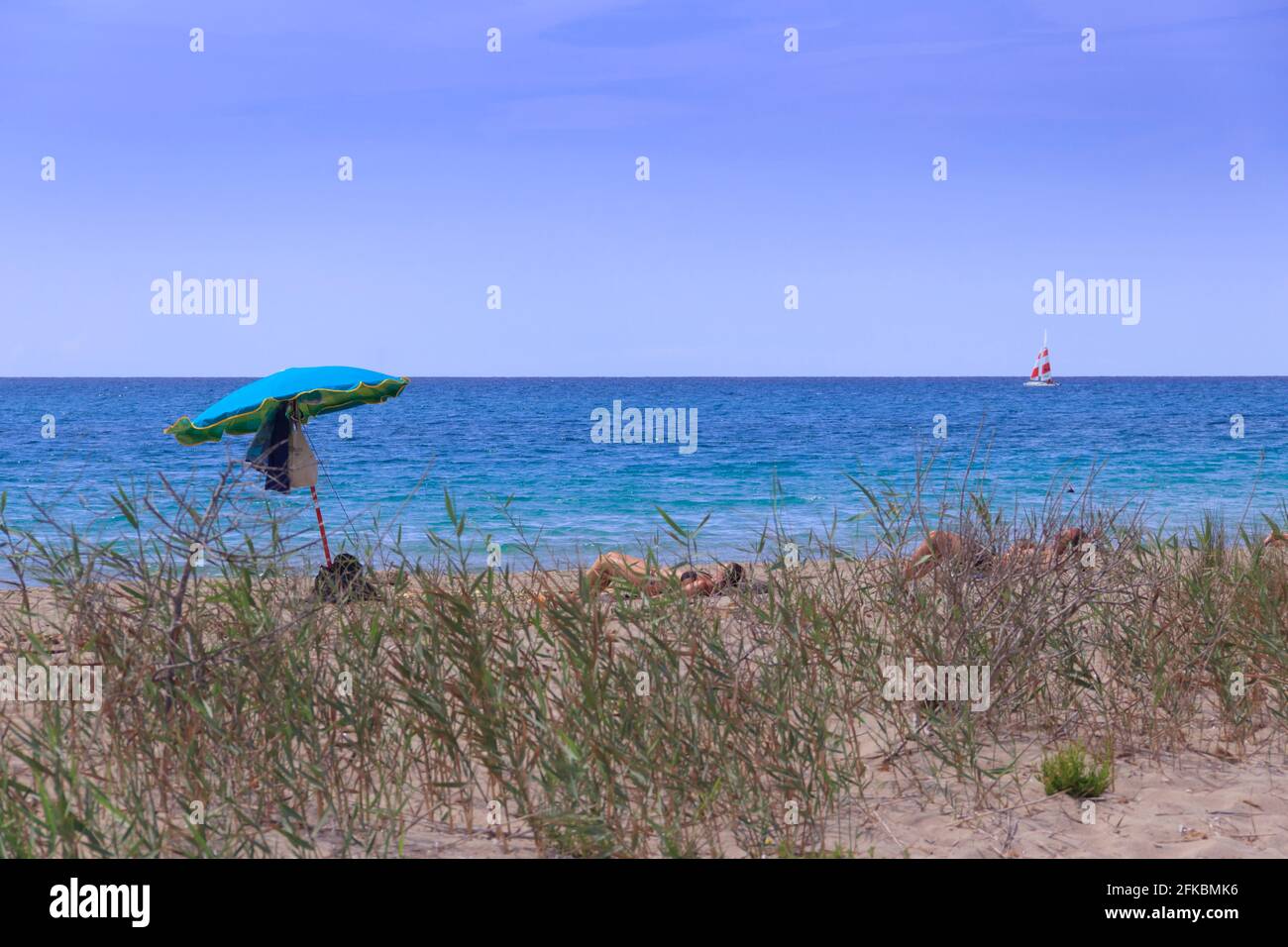 Relax on the beach, Apulia (Italy). Sunbathing tourists with lonely umbrella. Stock Photo