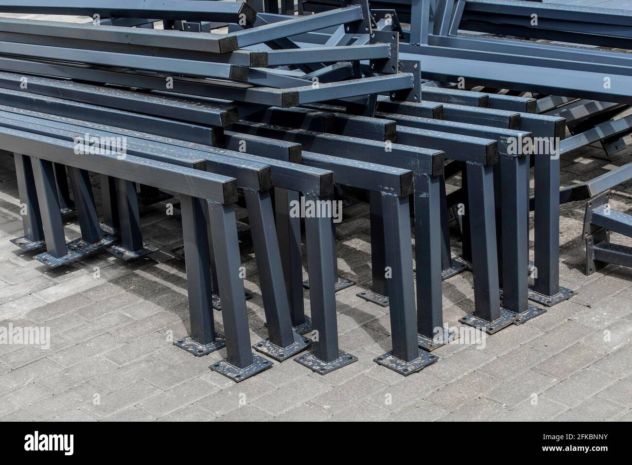 Pile of new metal structures or steel industrial material on paving slabs sidewalk at construction site. Stock Photo