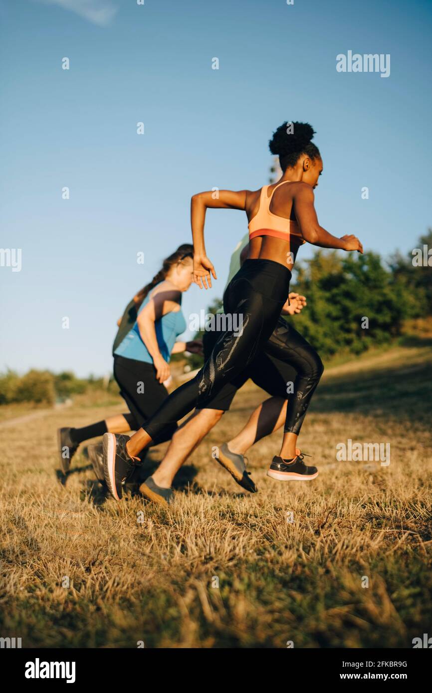 Male and female athletes running on grass against sky in park Stock Photo