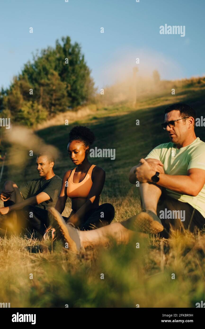 Male and female athletes meditating while sitting on grass in park ...