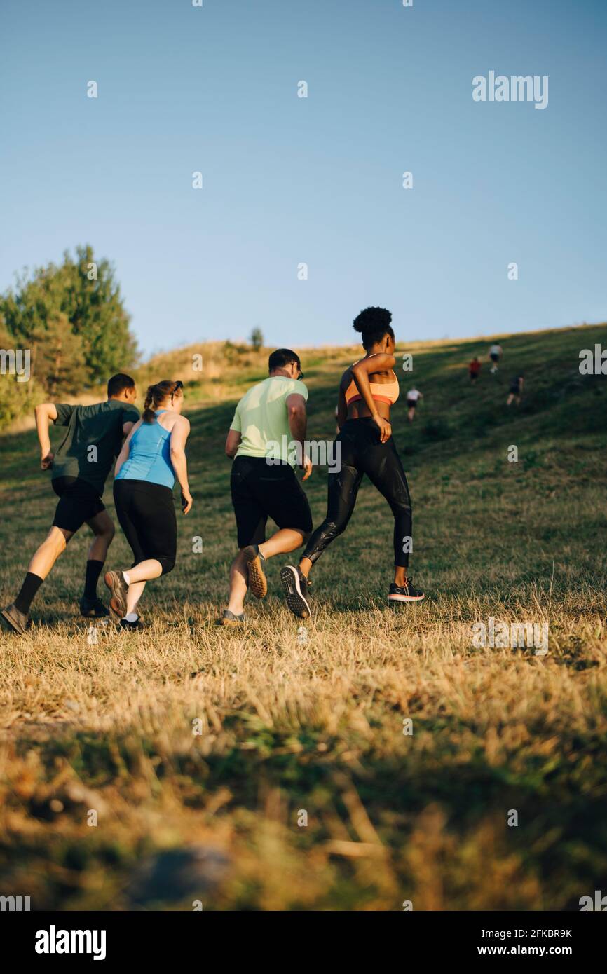 Rear view of male and female athletes running on grassy land Stock Photo