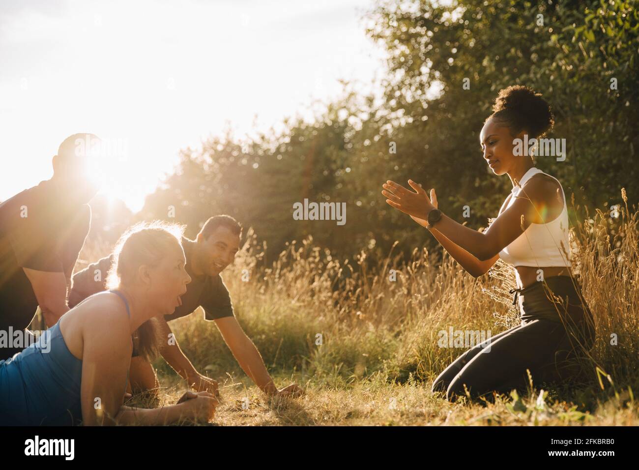 Male and female athletes exercising while fitness instructor cheering them in park Stock Photo
