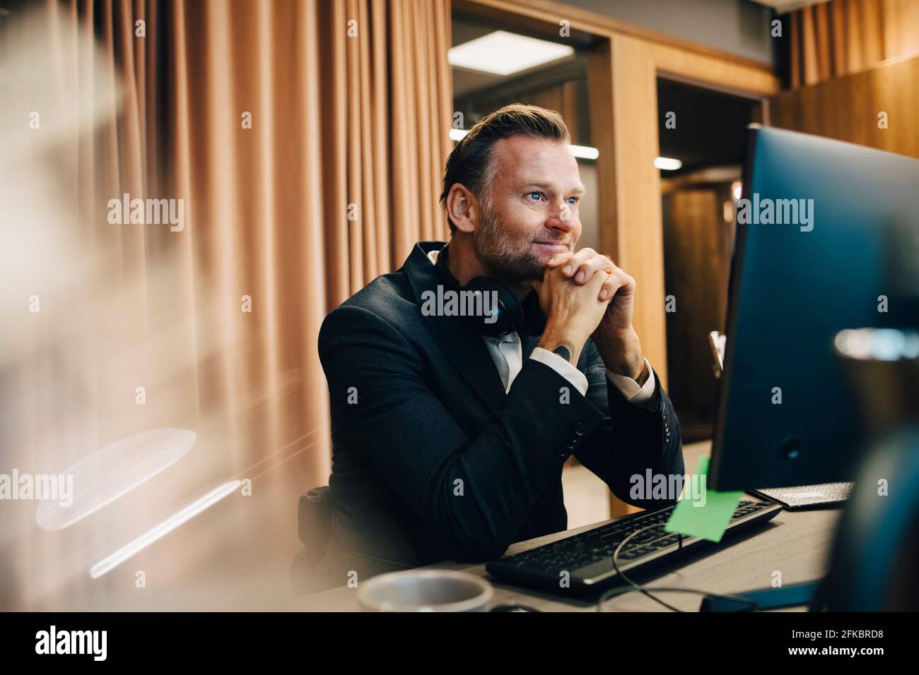 Smiling male entrepreneur with hand on chin working over laptop in office Stock Photo