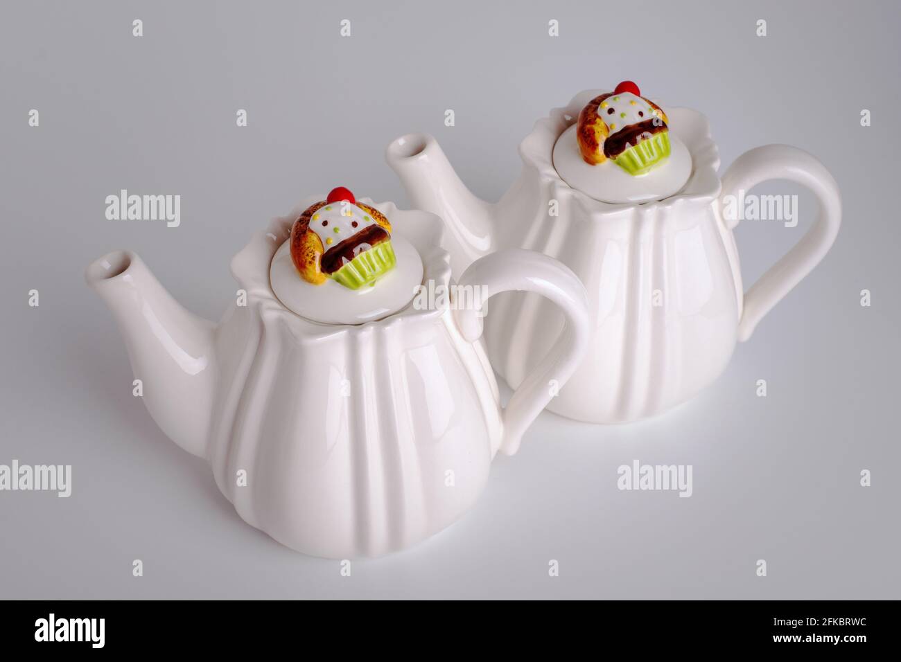 Two white teapots for tea. Dishes for tea drinking. Cupcake on a lid Muffin Stock Photo