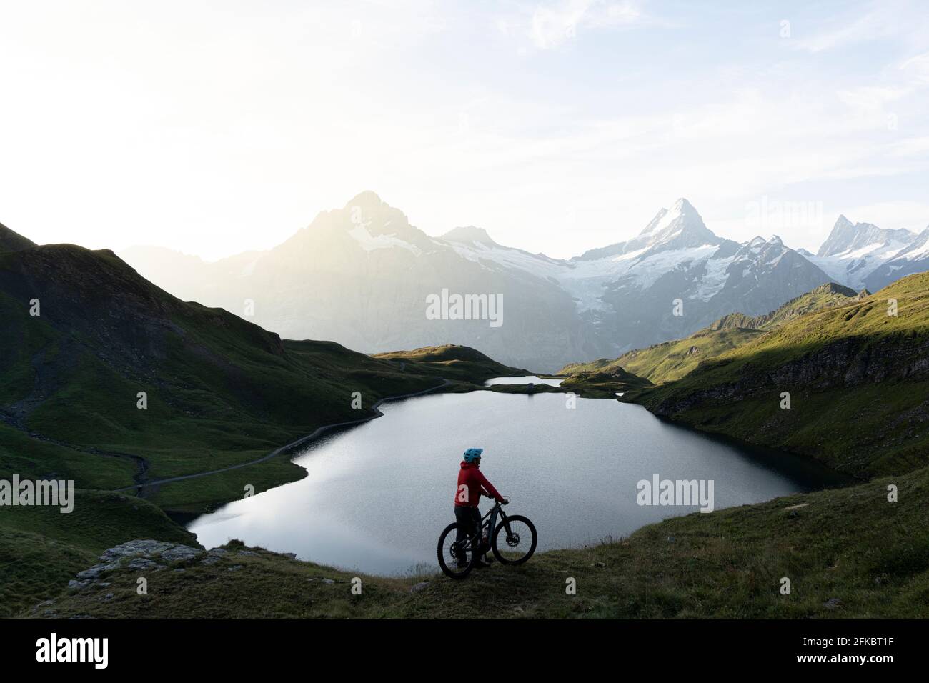 Hiker with mountain bike admiring sunrise over Bachalpsee lake, Grindelwald, Bernese Oberland, Bern Canton, Switzerland, Europe Stock Photo