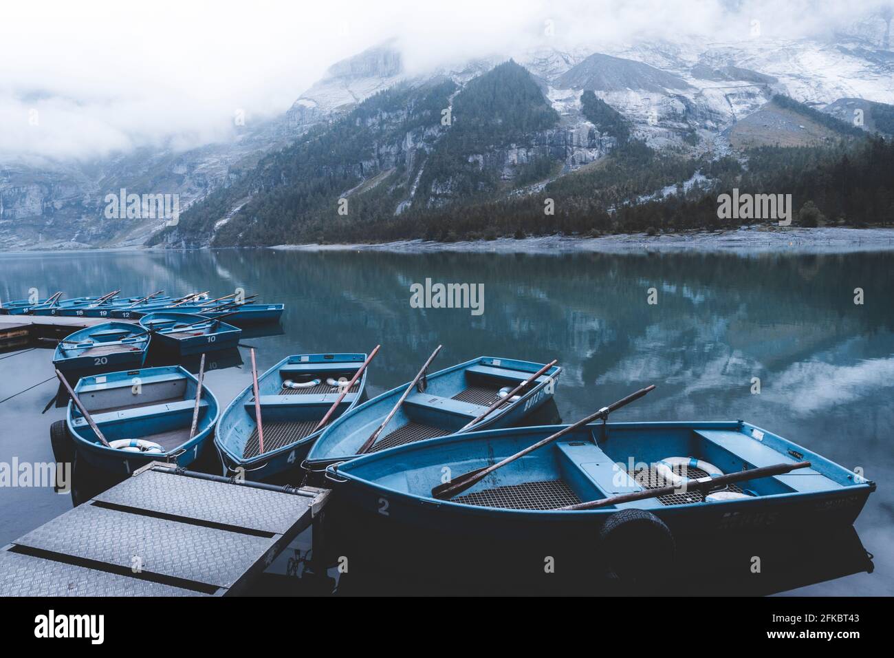 Row boats moored on shore of lake Oeschinensee on a foggy day, Bernese Oberland, Kandersteg, Bern canton, Switzerland, Eurpe Stock Photo