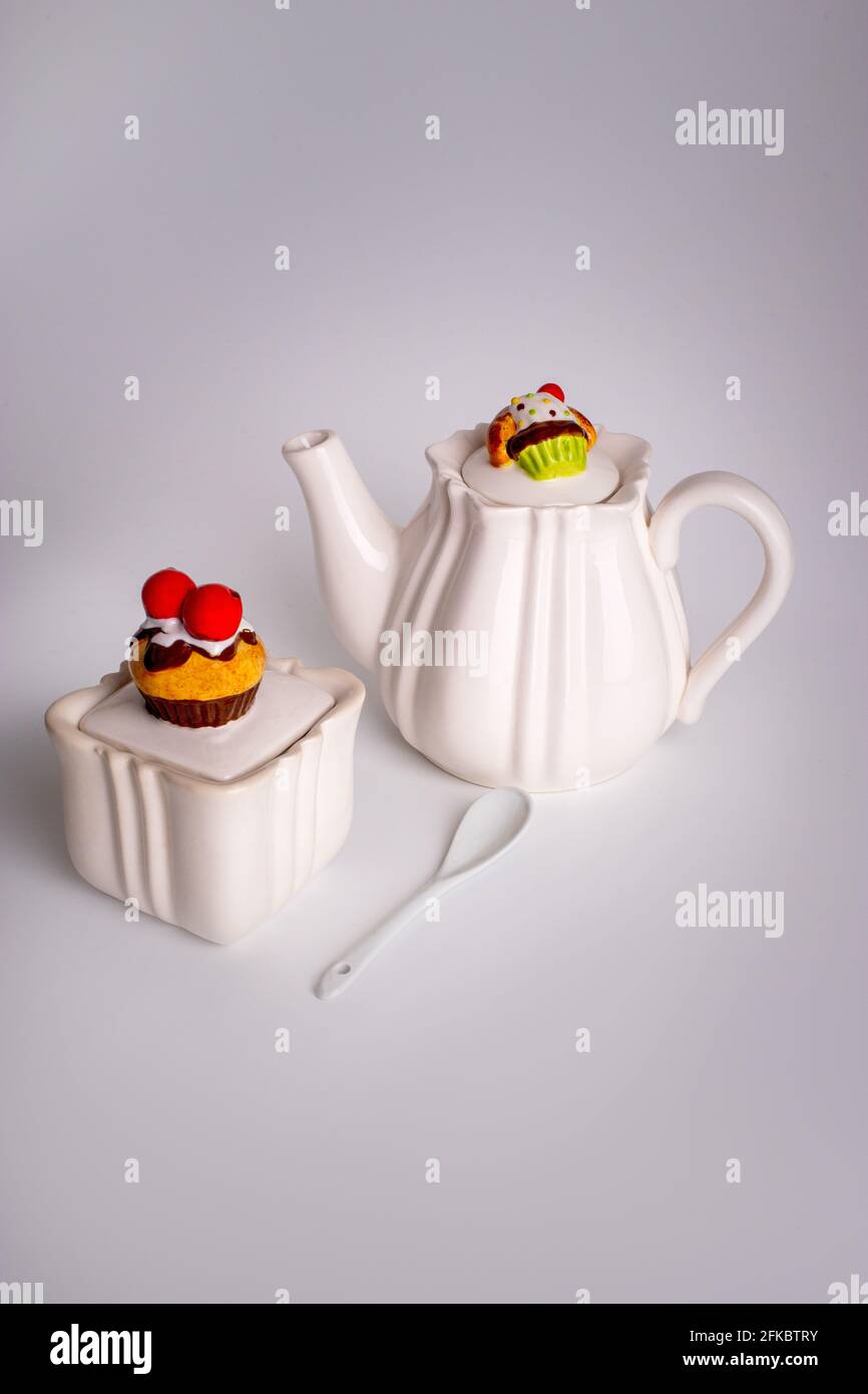 White ceramic teapot with sweets decor. Sugar bowl with a cupcake. Cake on the teapot lid. Ceramic tableware Stock Photo
