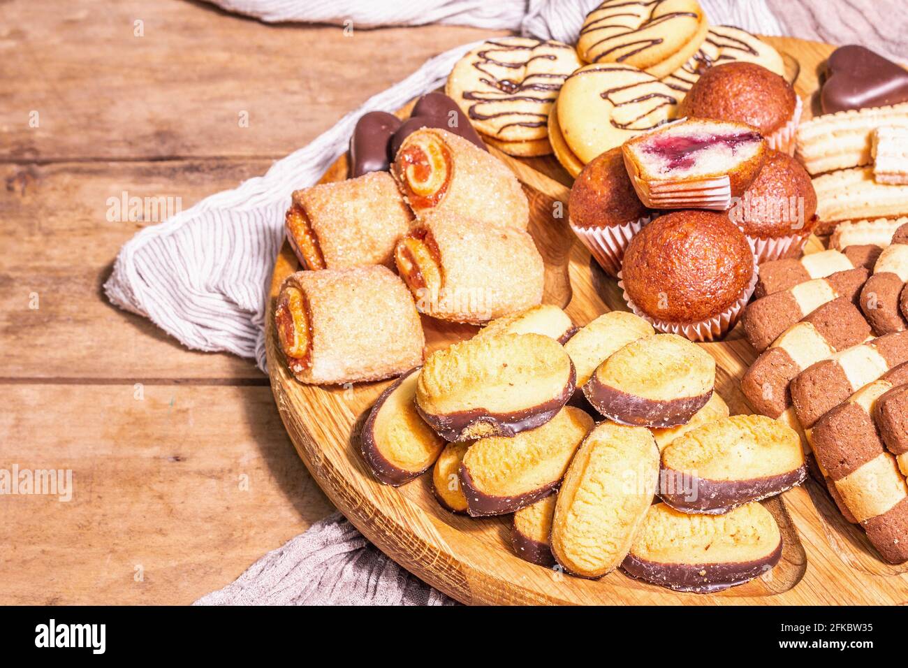 Assorted various cookies and muffins. Trendy hard light, dark shadow. Wooden combination plate on old boards table, close up Stock Photo