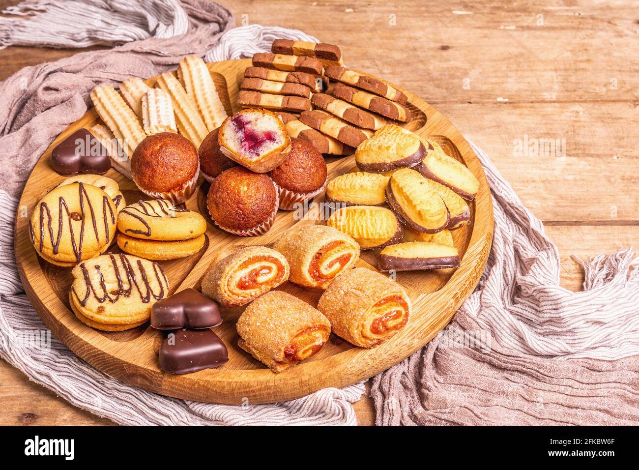 Assorted various cookies and muffins. Wooden combination plate on old boards table, close up Stock Photo