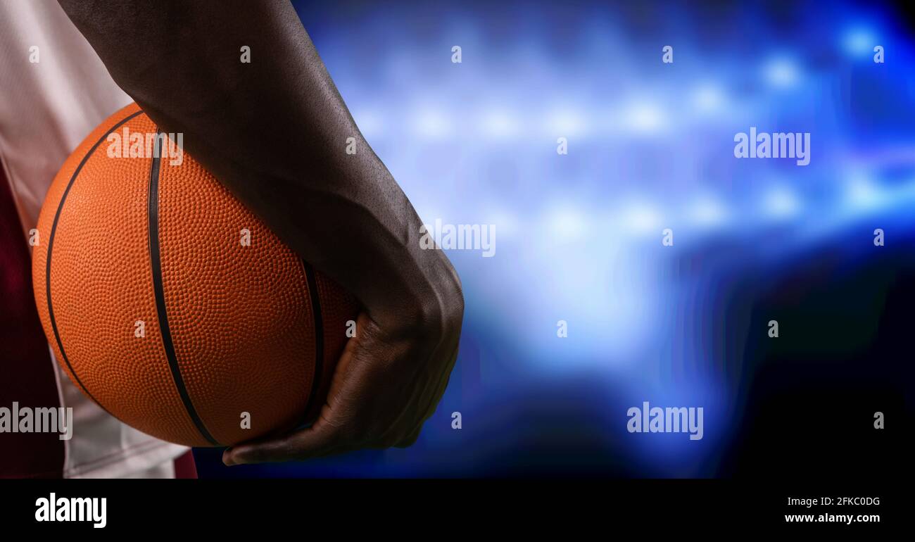Composition of midsection of basketball player holding basketball over blue spotlights Stock Photo
