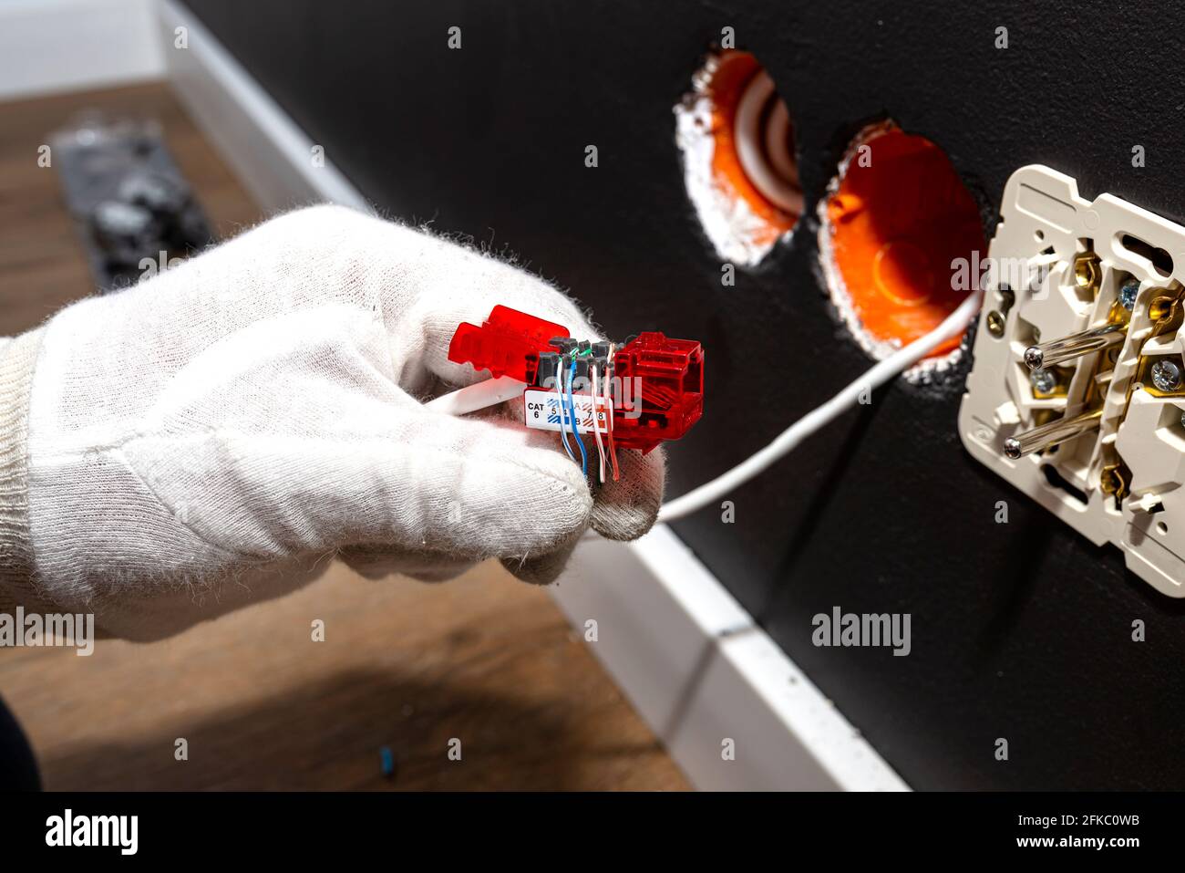 An electrician in white gloves is installing a network cable for the RJ45 module to the computer socket in the room. Stock Photo