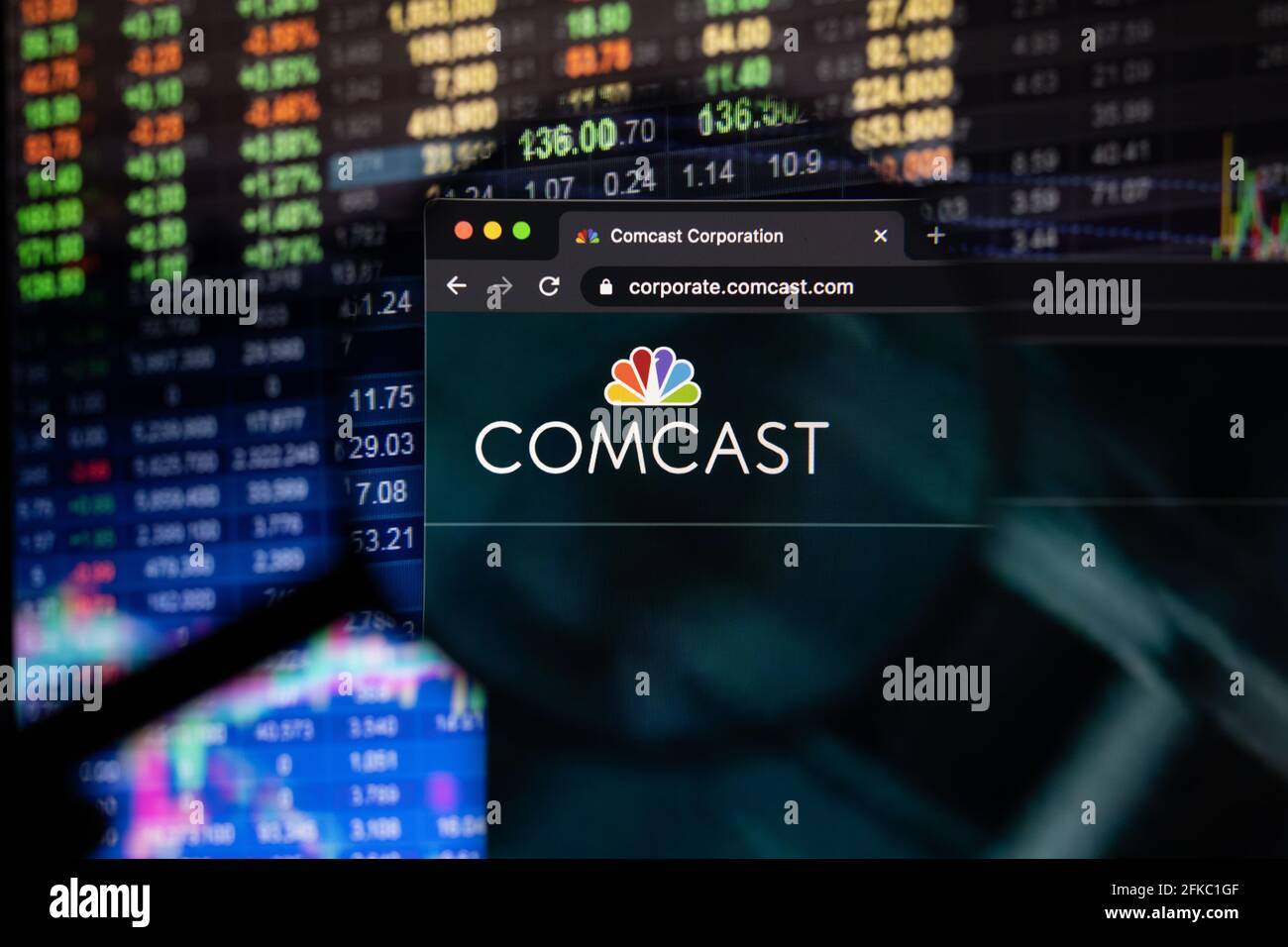 Comcast company logo on a website with blurry stock market developments in the background, seen