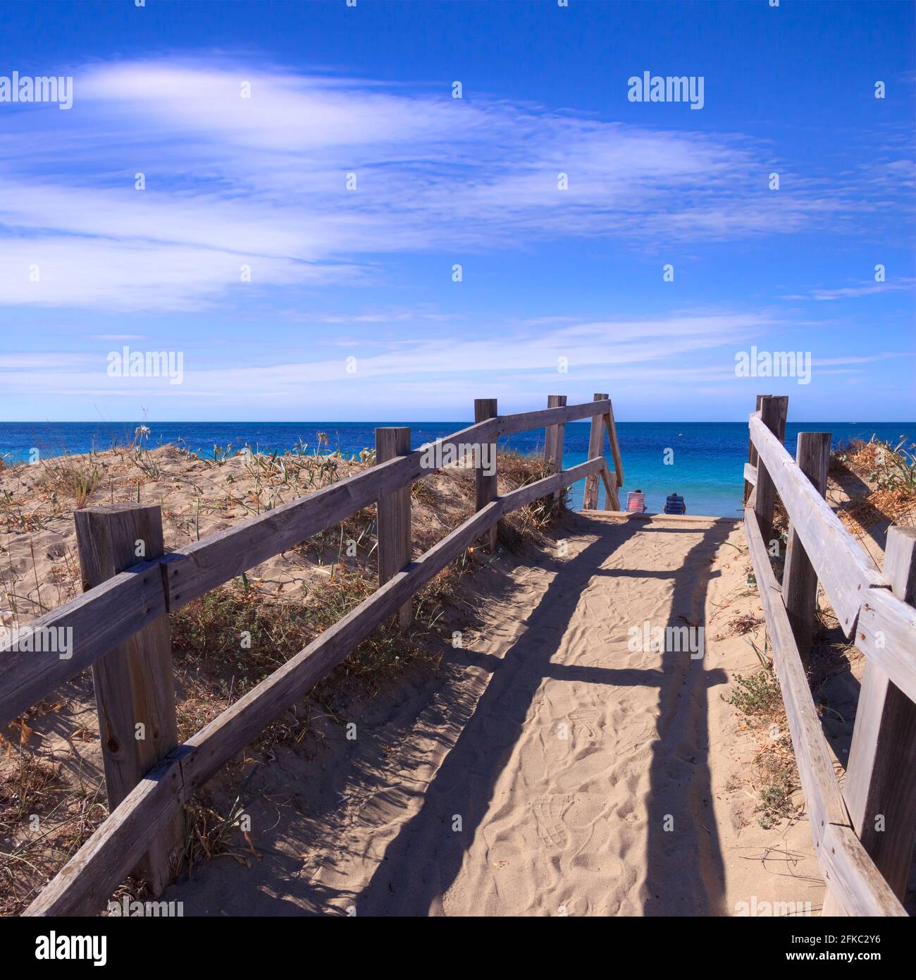 Boardwalk on the beach: fence between sea dunes in Salento, Apulia (Italy). Tourists sitting on deck chairs. Stock Photo