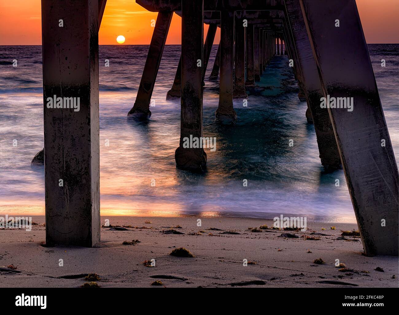 Sun rises between the concrete pillars of the Deerfield Beach International Fishing Pier Stock Photo
