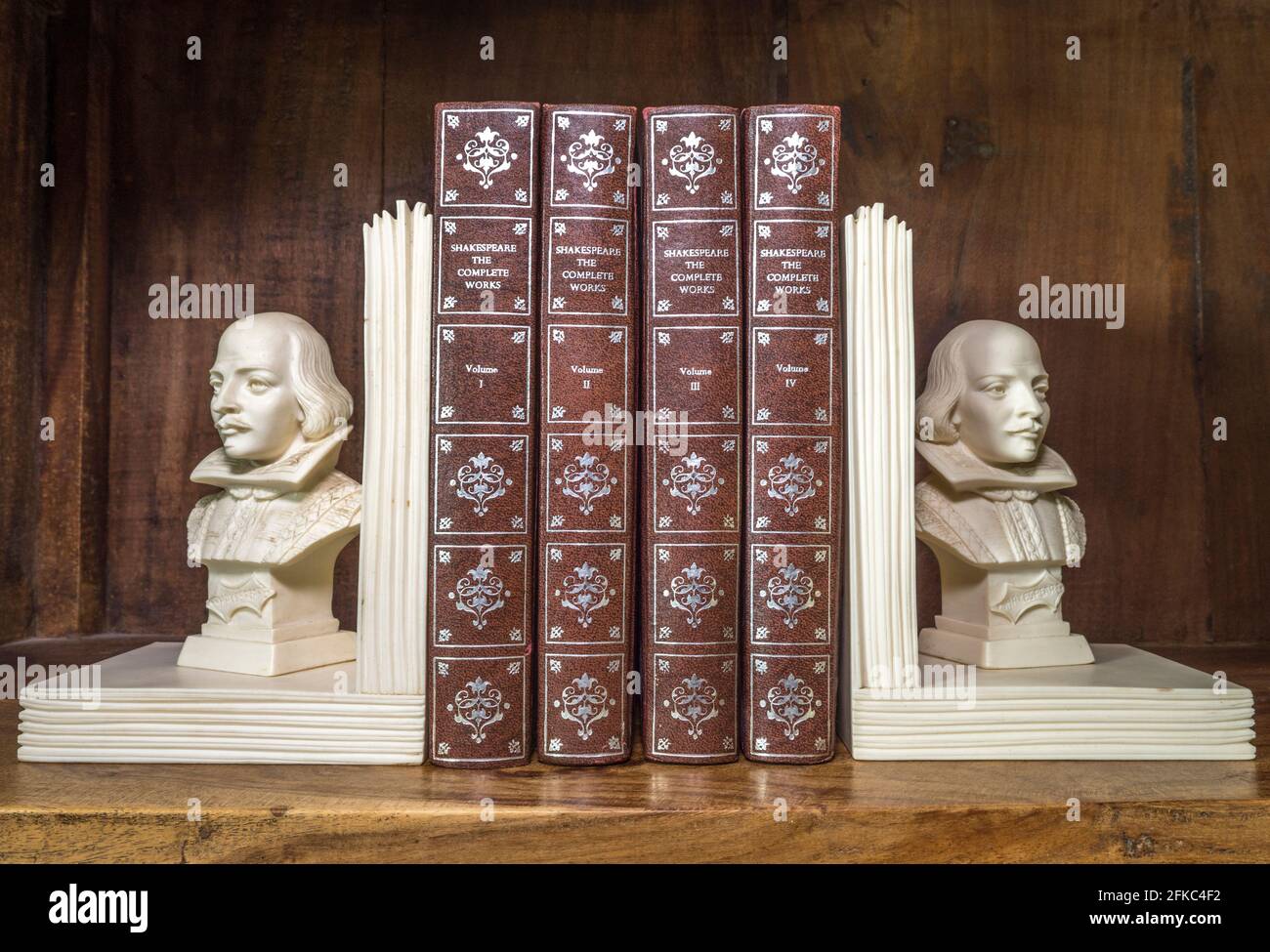 The Complete Works of Shakespeare books, between two William Shakespeare bust ornament bookends, on a shelf in a traditional old wooden bookcase. Stock Photo