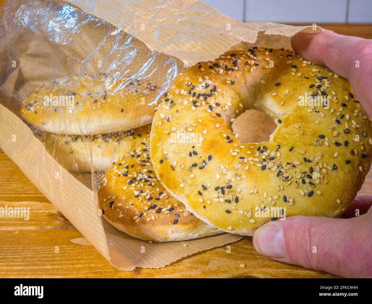 Closeup of finger and thumb taking a fresh Persian barbari bread, in a bagel shape, topped with nigella and sesame seeds, from four in a paper packet. Stock Photo
