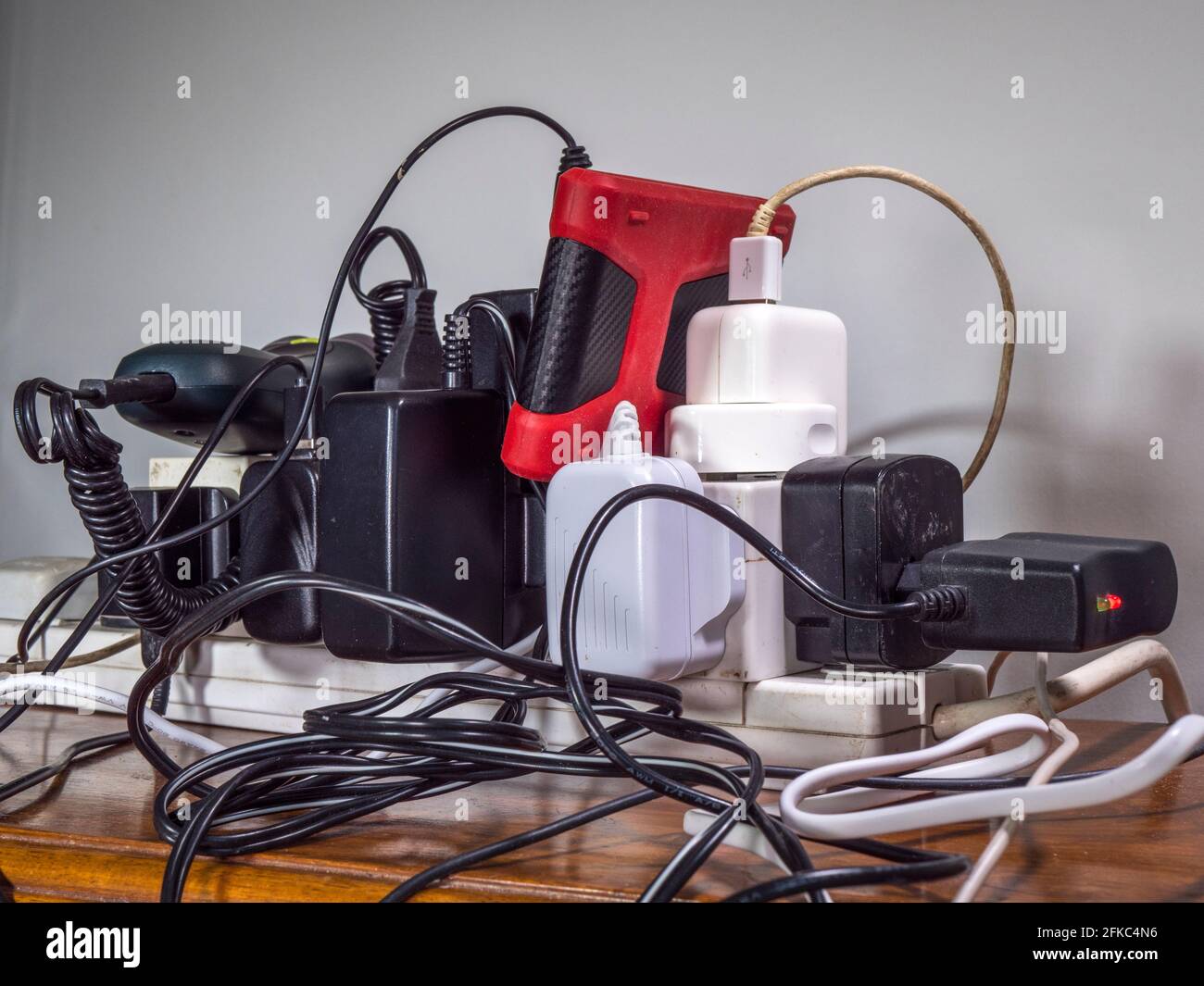 Unsafe, overloaded, UK 240 volt electricity supply, with a mess of plugs, sockets, extensions, wires and cables, all plugged into an extension board. Stock Photo