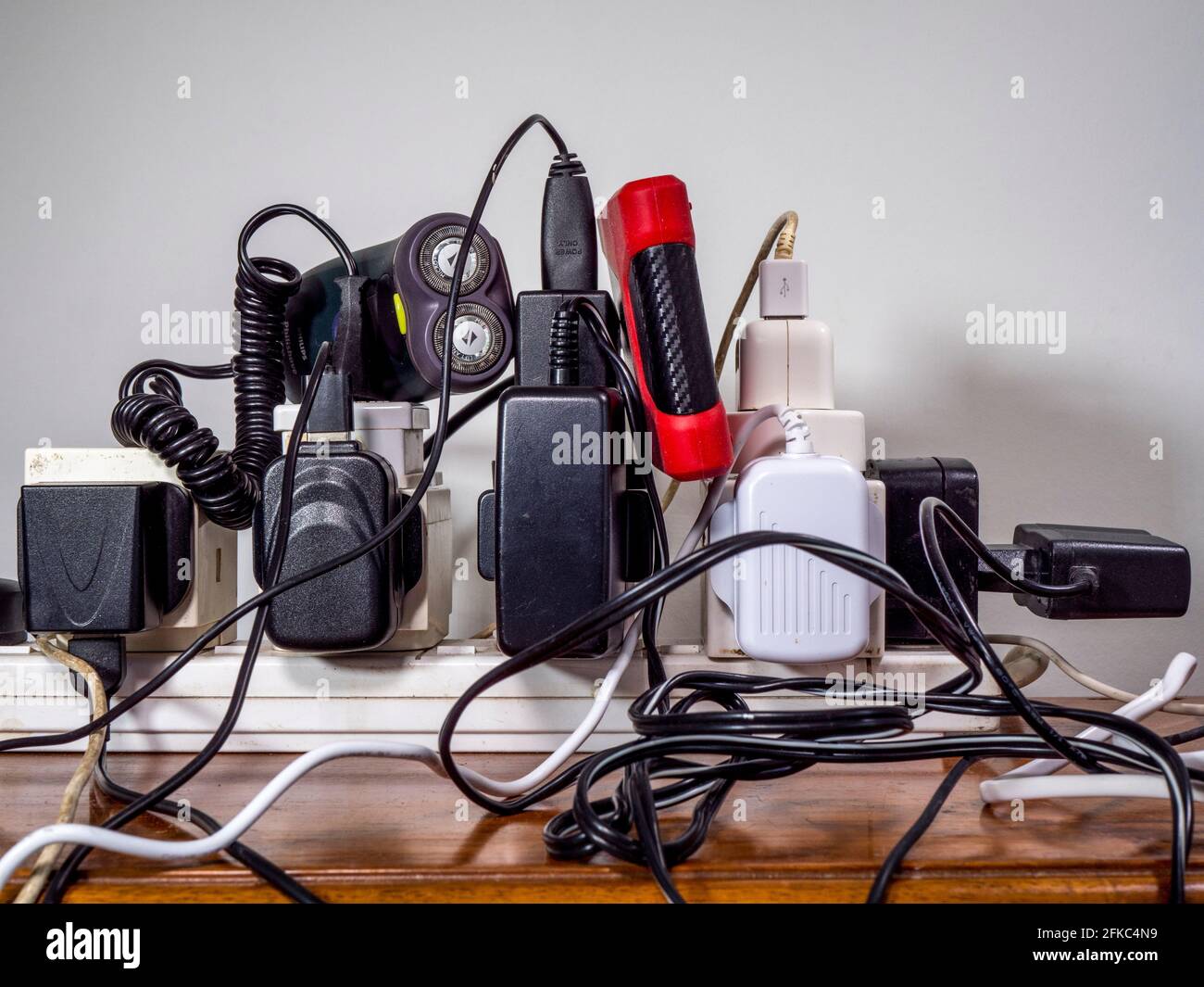 Unsafe, overloaded, UK 240 volt electricity supply, with a mess of plugs, sockets, extensions, wires and cables, all plugged into an extension board. Stock Photo