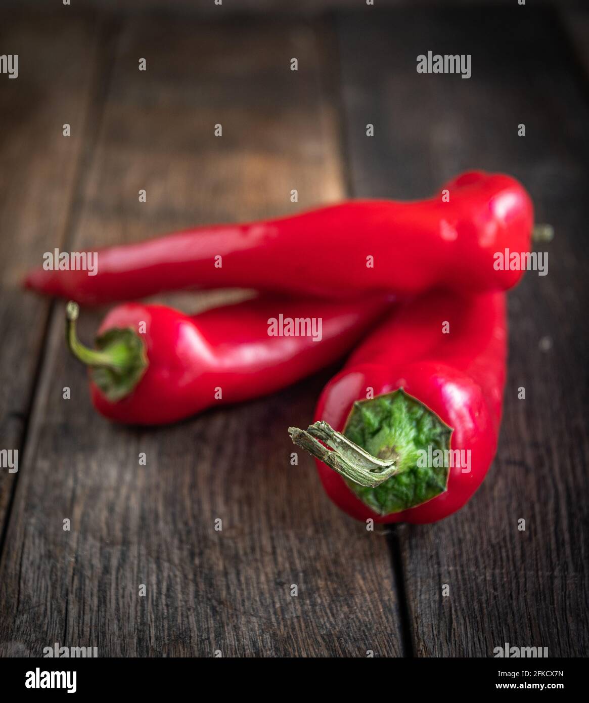 Three appetizing red peppers on a ceramic plate, on a wooden kitchen ...
