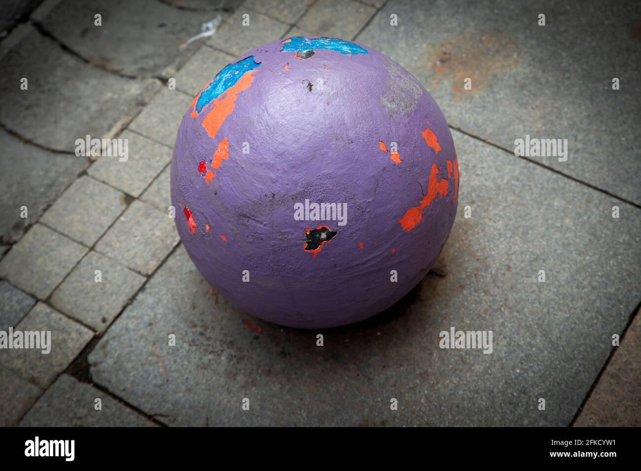 Close up high angle view image of a Colorful concrete ball on dull grey pavement, with worn out colorful layers of paint. Stock Photo