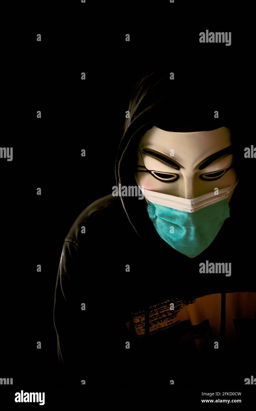 Man wearing Vendetta mask and medical face mask isolated on black. Stock Photo