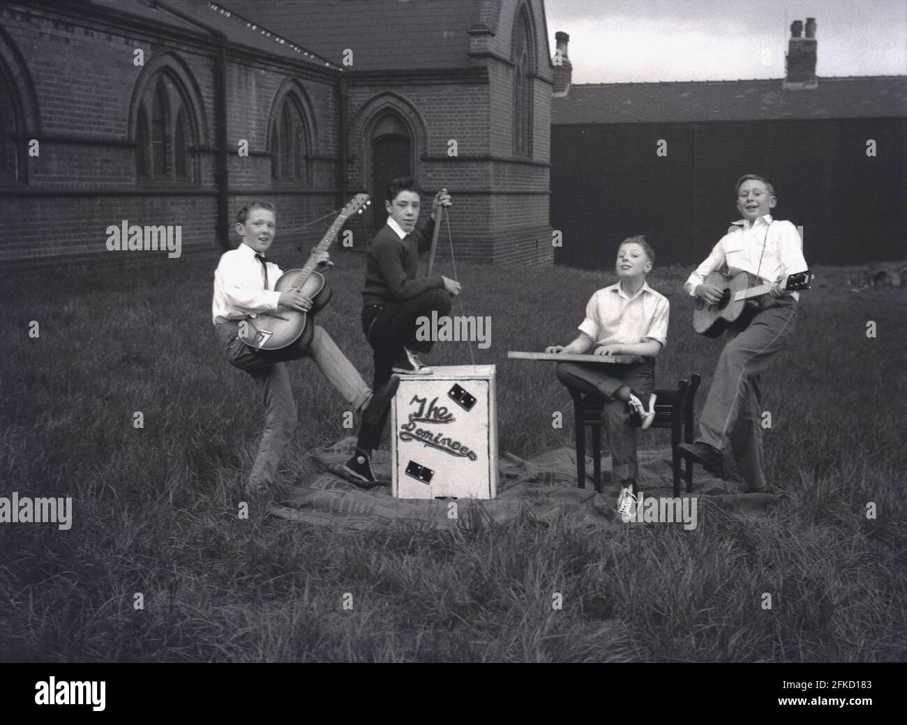 1958, historical, outside in the grounds of a Church, four young lads from the skiffle band, The Dominoes, pose for a picture with their musical instruments, guitars and a washboard, before taking part in the May Queen Carnival. In Britain, May Day was an ancient tradition which celebrated the arrival of Spring and Summer. In many British northern towns, the parade was connected to the Church of England Sunday school. The figure of the May Queen and her purity is linked to ancient worship and folklore. Stock Photo