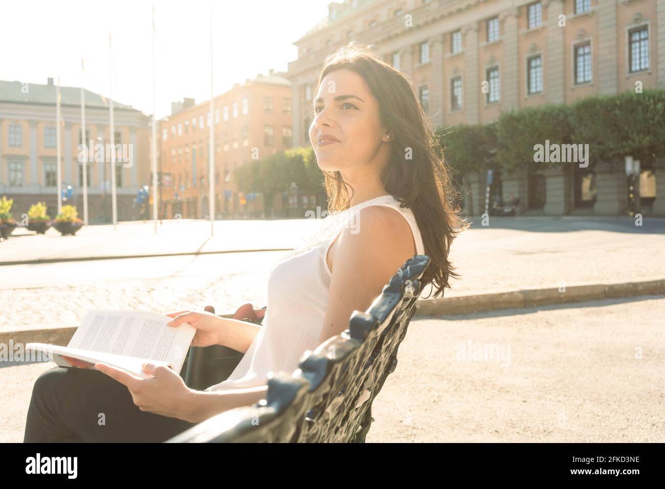 Sweden, Stockholms Lan, Stockholm, Young woman sitting on bench and holding book Stock Photo