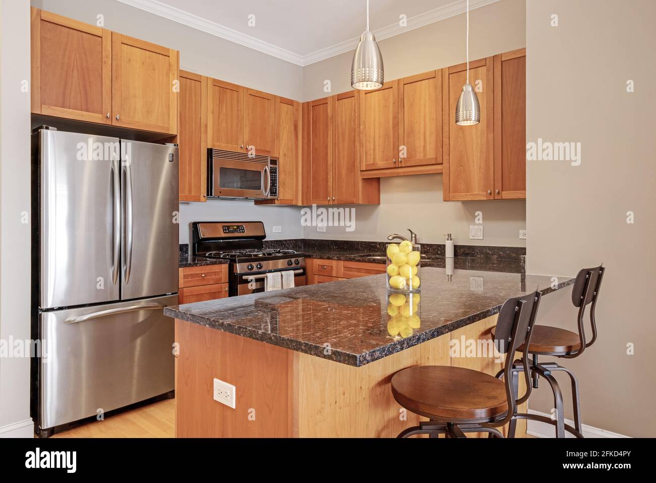An Apartment Kitchen With Maple Cabinets Black Granite Countertops Stainless Appliances And Pendant Lights And Bar Stools Stock Photo Alamy