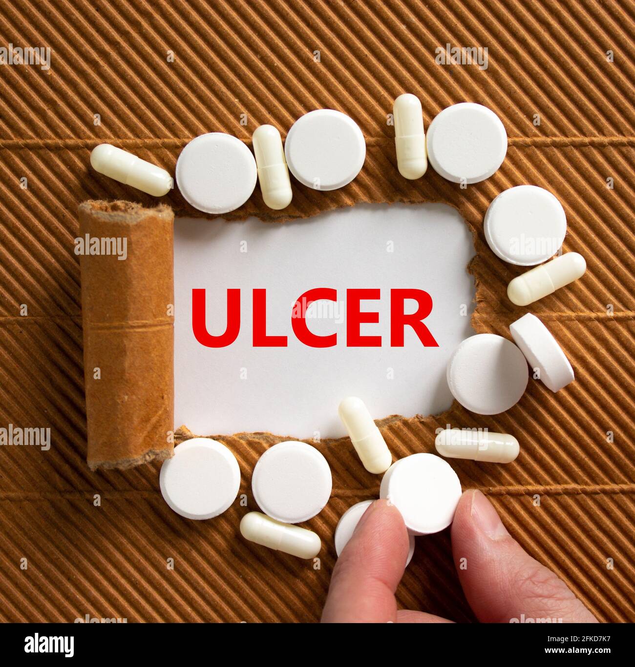 Stomach ulcer symbol. The word 'ulcer' appearing behind torn brown paper, white pills. Doctor hand. Medical and stomach ulcer concept. Copy space. Stock Photo