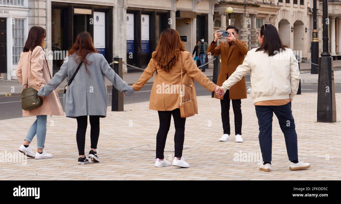 Four female friends holding hands in Pall Mall having their photo taken Stock Photo