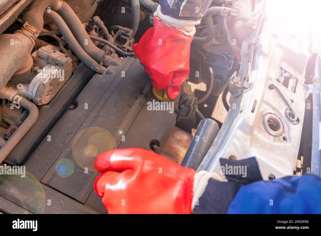 A man in red rubber gloves changes the oil in a car engine. Car repair with the hood up  Stock Photo