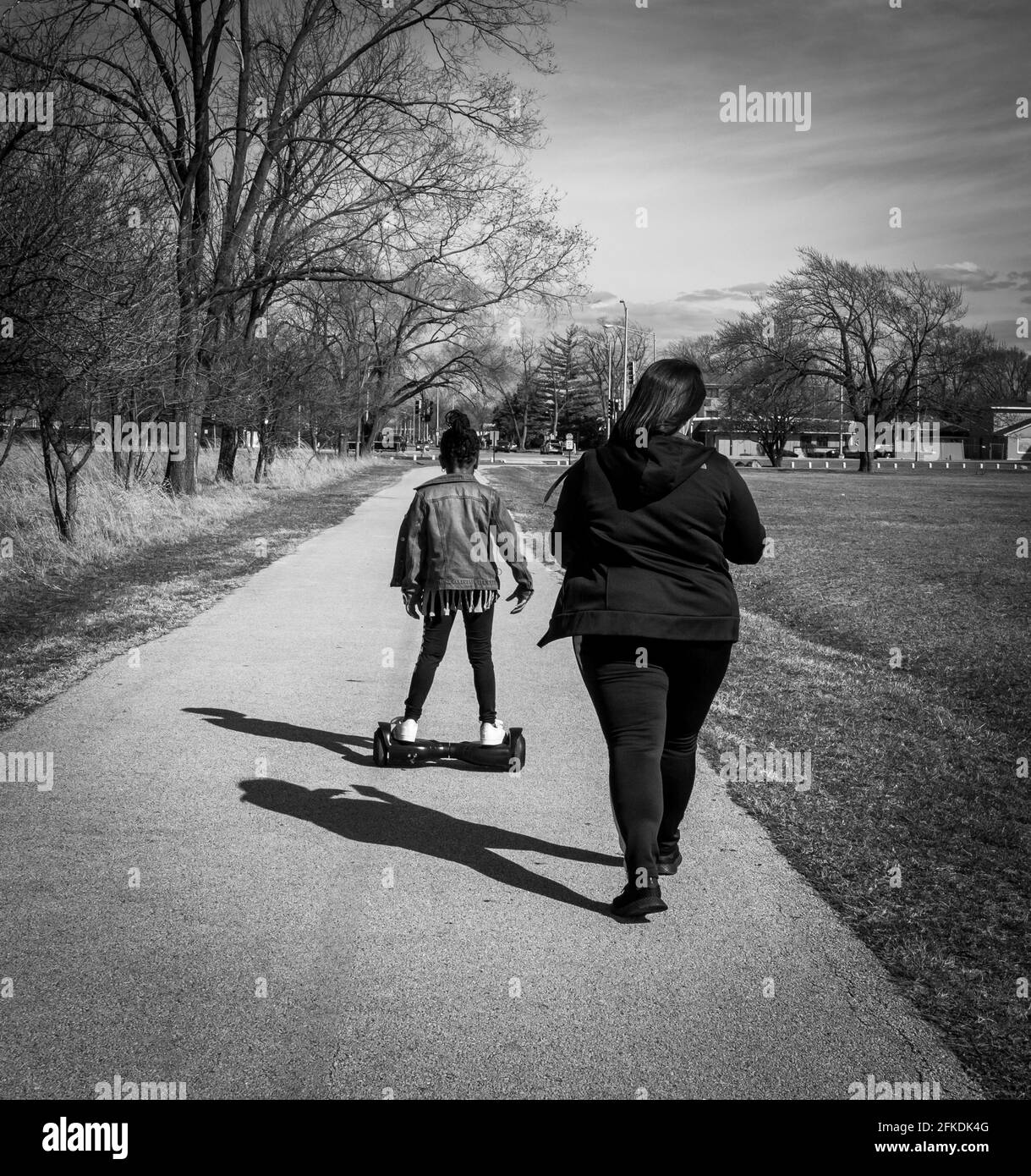 RIVERDAE, ILL. USA MARCH 22, 2021: AN AFRICAN AMERICAN WOMAN AND    YOUNG GIRL WALKING ON A TRAIL IN THE PARK, THE GIRL IS ON A HOVER BOARD Stock Photo