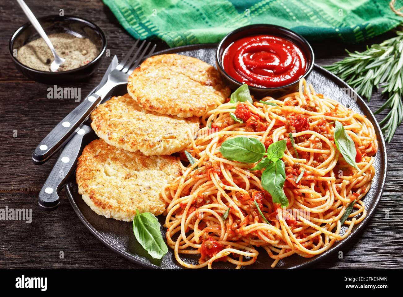 cod fish patties served on a black plate with spaghetti mixed with lentils, tomato sauce and herbs, horizontal view from above Stock Photo