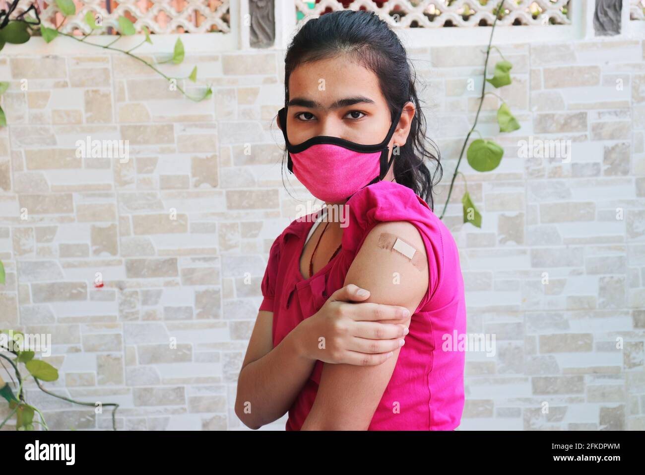 Indian girl shows a bandage applied after getting vaccination during new strain of covid-19, young teenager wearing mask received a coronavirus vaccin Stock Photo