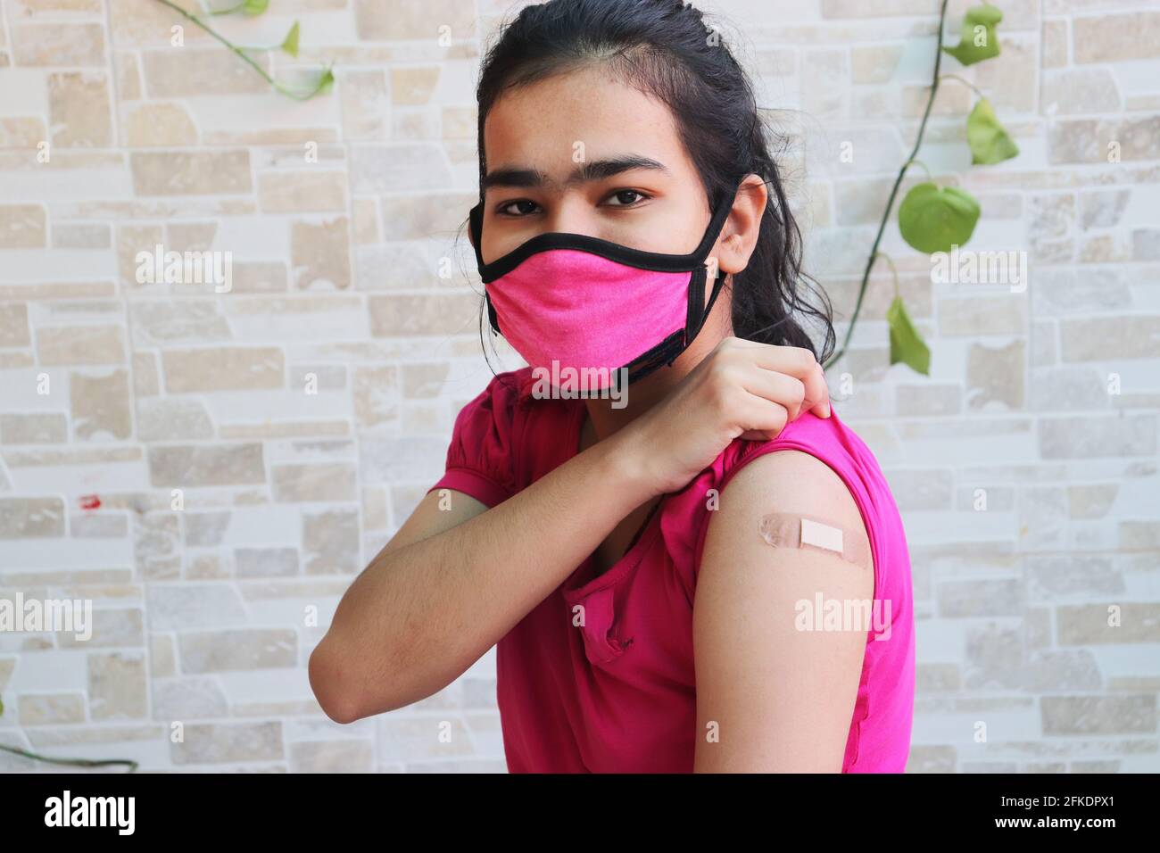 Indian girl shows a bandage applied after getting vaccination during new strain of covid-19, young teenager wearing mask received a coronavirus vaccin Stock Photo