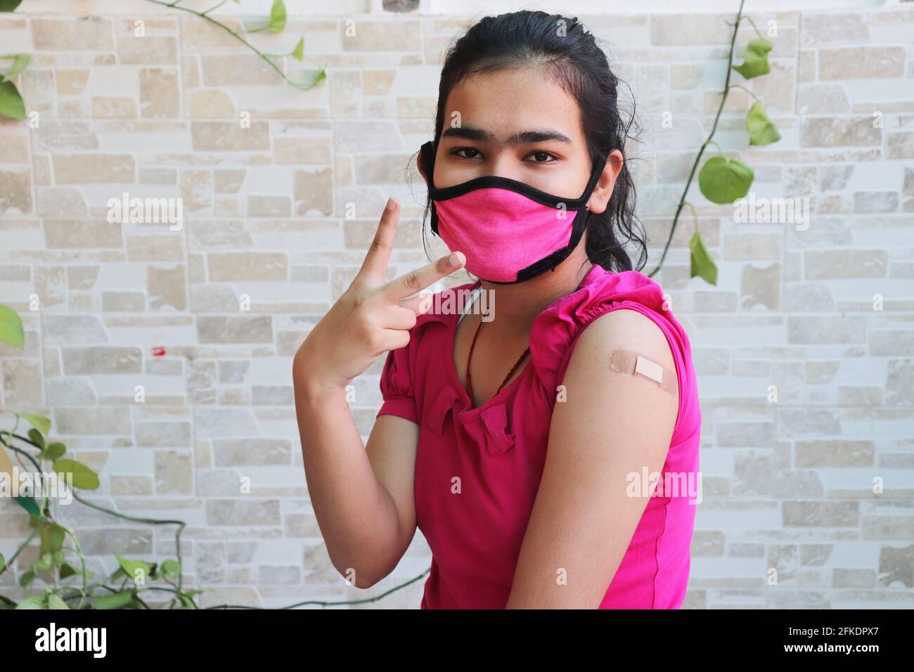 Indian girl do victory Sign after getting vaccination during new strain of covid-19, Young female wearing mask with bandage applied received a coronav Stock Photo