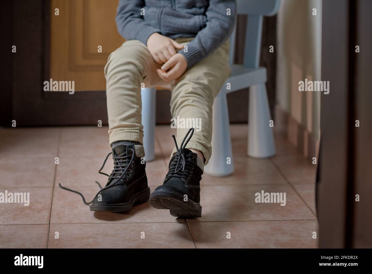 Child learning to tie shoelaces on boots before leaving home, selective focus Stock Photo